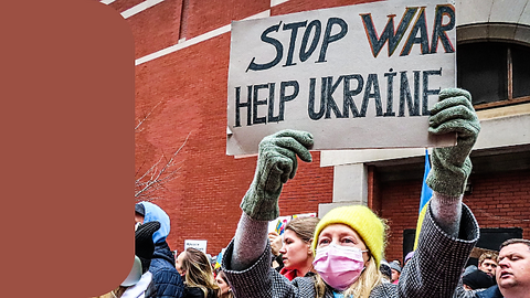 Eine Frau mit gelber Mütze zeigt ein Schild. Darauf steht Stop war, help Ukraine.