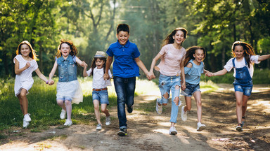 Kinder laufen frohlich durch den Wald und halten sich dabei an den Händen fest.